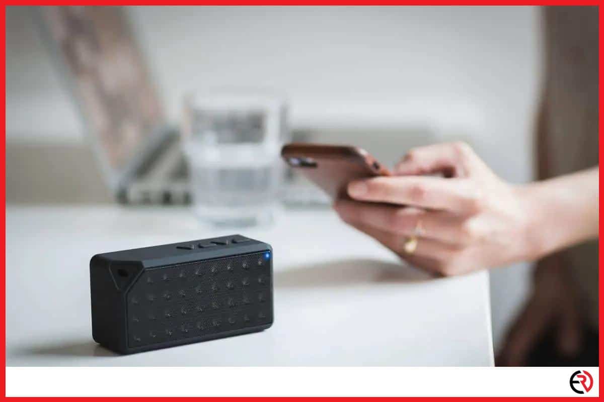 Person holding an iPhone beside a Bluetooth speaker